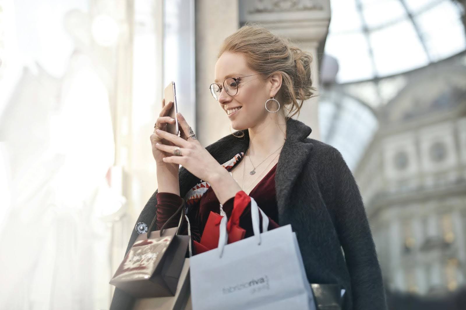 a woman holding her phone with shopping bags on her arm