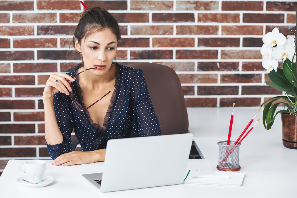 Business woman in the office at the desk with laptop thinking