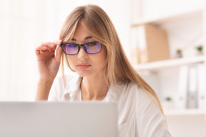 Businesswoman Looking Through Eyeglasses At Laptop Sitting In Office